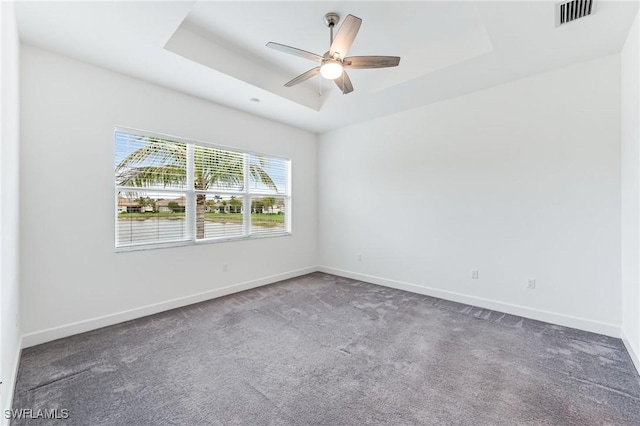 carpeted empty room with visible vents, a ceiling fan, a raised ceiling, and baseboards