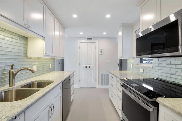 kitchen with stainless steel appliances, light stone countertops, sink, and white cabinets