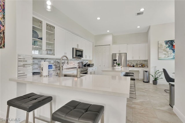 kitchen with white cabinetry, stainless steel appliances, a kitchen breakfast bar, kitchen peninsula, and decorative backsplash