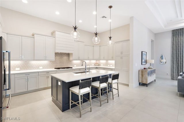 kitchen featuring pendant lighting, sink, stainless steel refrigerator, a kitchen island with sink, and backsplash