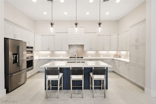 kitchen with decorative light fixtures, a center island with sink, white cabinets, and appliances with stainless steel finishes