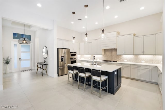 kitchen featuring white cabinetry, stainless steel appliances, a kitchen breakfast bar, a center island with sink, and decorative light fixtures