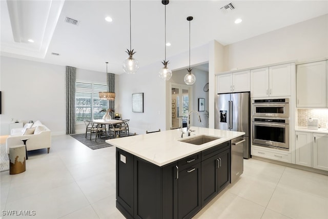 kitchen with appliances with stainless steel finishes, decorative light fixtures, white cabinetry, sink, and a kitchen island with sink