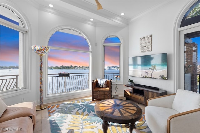 sitting room featuring beamed ceiling, light wood-type flooring, ornamental molding, and a wealth of natural light