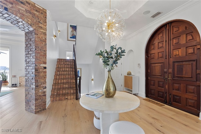 entryway with a raised ceiling, light hardwood / wood-style floors, crown molding, and a notable chandelier