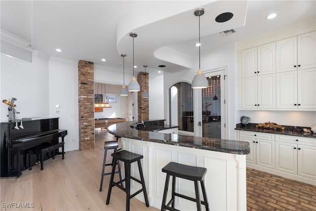 kitchen featuring pendant lighting, dark stone counters, white cabinets, a kitchen breakfast bar, and ornamental molding