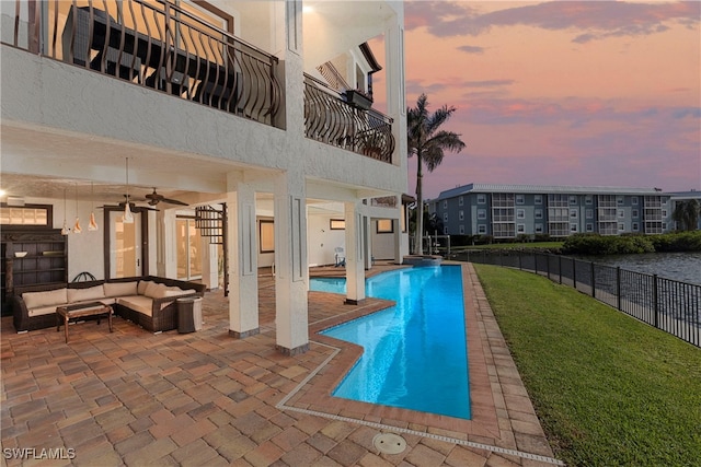 pool at dusk with a yard, an outdoor living space, a patio, and ceiling fan