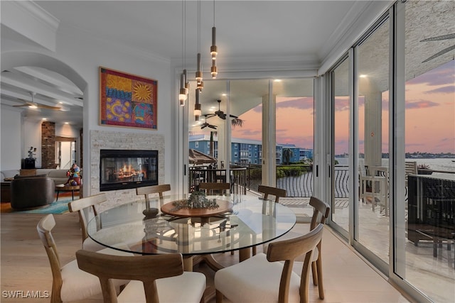 dining area with a stone fireplace, ornamental molding, and light wood-type flooring