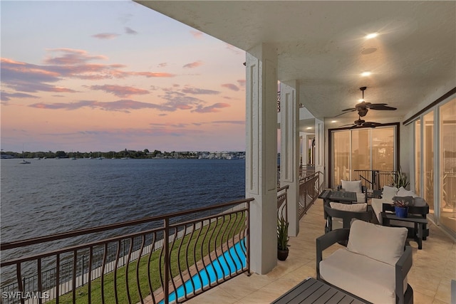 balcony at dusk featuring ceiling fan, a water view, and an outdoor living space