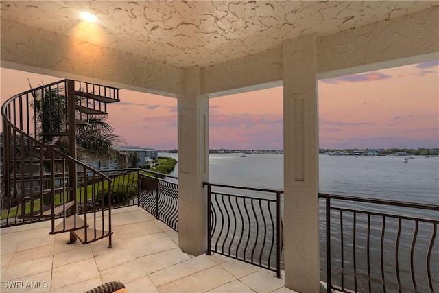 balcony at dusk featuring a water view