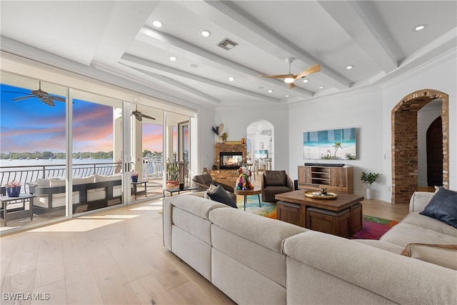 living room featuring a fireplace, beamed ceiling, light hardwood / wood-style floors, and ornamental molding