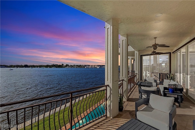 balcony at dusk featuring ceiling fan and a water view