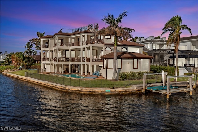 back house at dusk with a yard, a balcony, a patio area, and a water view