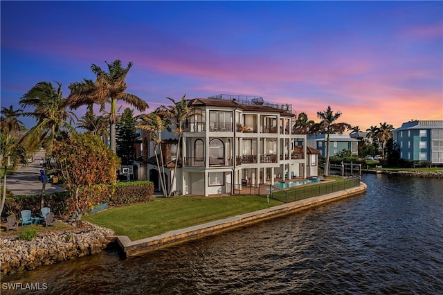 back house at dusk with a balcony, a patio area, a yard, and a water view