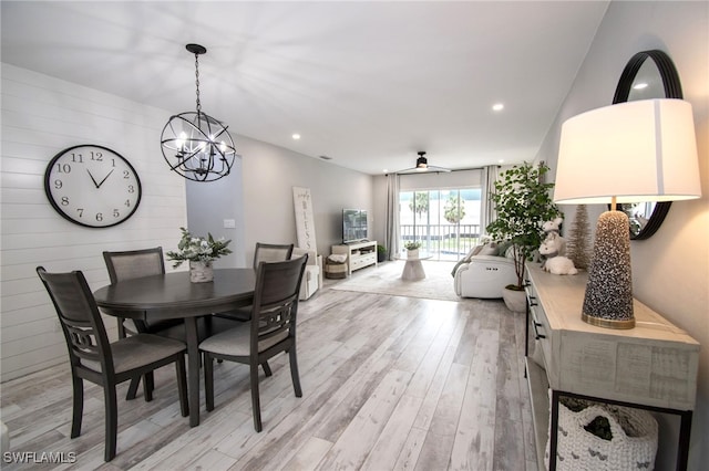 dining area with ceiling fan with notable chandelier, wood walls, and light wood-type flooring