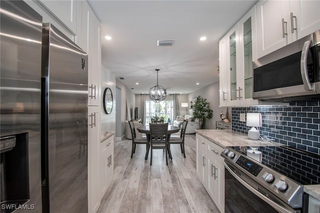 kitchen with light stone counters, white cabinets, stainless steel appliances, and light hardwood / wood-style floors