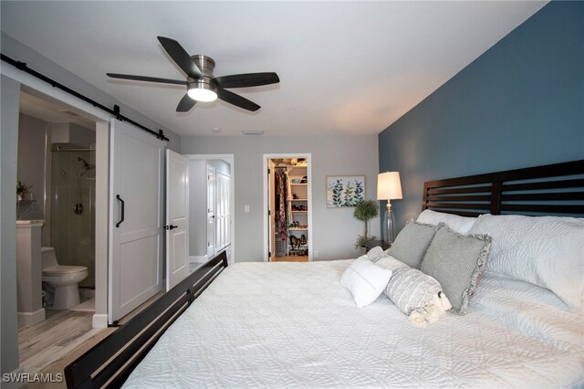 bedroom with ceiling fan, a barn door, a spacious closet, connected bathroom, and a closet