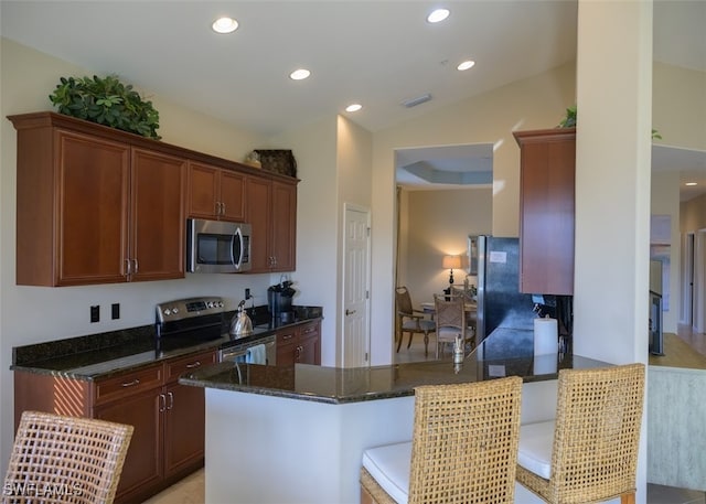 kitchen featuring kitchen peninsula, dark stone countertops, vaulted ceiling, a breakfast bar, and appliances with stainless steel finishes