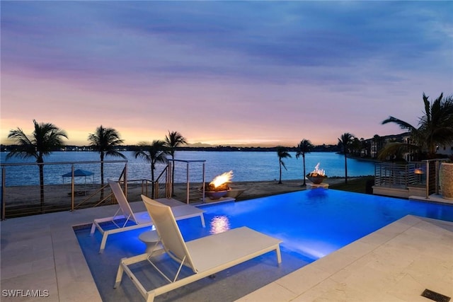 pool at dusk featuring a water view, a patio, and an outdoor fire pit