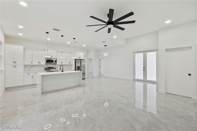 kitchen with appliances with stainless steel finishes, french doors, a center island with sink, white cabinetry, and hanging light fixtures