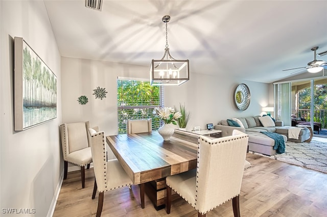 dining area with ceiling fan with notable chandelier, light hardwood / wood-style flooring, and plenty of natural light