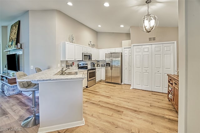 kitchen featuring kitchen peninsula, appliances with stainless steel finishes, a kitchen bar, light wood-type flooring, and decorative light fixtures