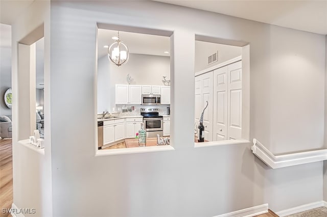 kitchen with stainless steel appliances, sink, a notable chandelier, white cabinets, and hanging light fixtures