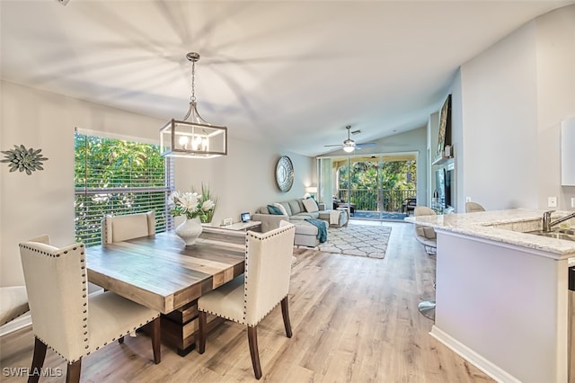 dining room with ceiling fan with notable chandelier, light hardwood / wood-style flooring, a wealth of natural light, and lofted ceiling