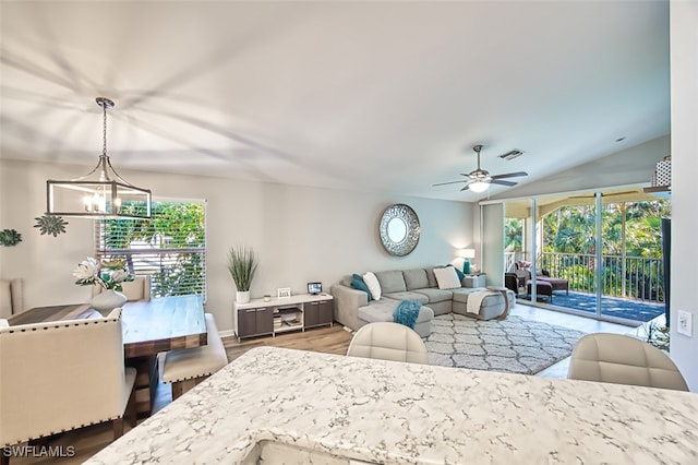 living room with ceiling fan with notable chandelier, vaulted ceiling, and hardwood / wood-style flooring