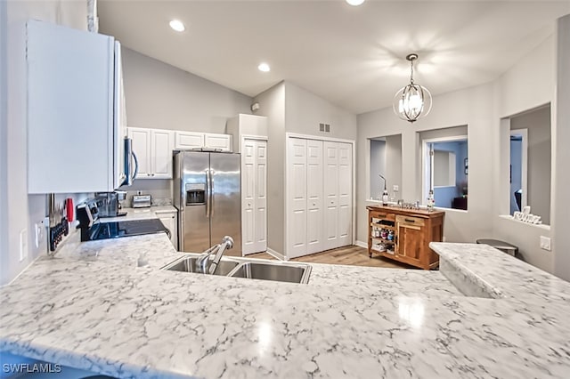 kitchen with appliances with stainless steel finishes, vaulted ceiling, sink, white cabinetry, and hanging light fixtures