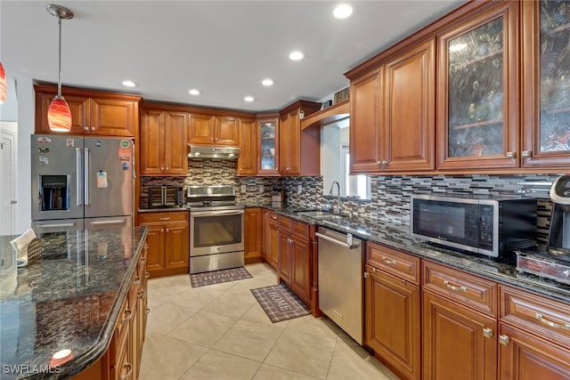 kitchen with pendant lighting, backsplash, dark stone counters, sink, and appliances with stainless steel finishes