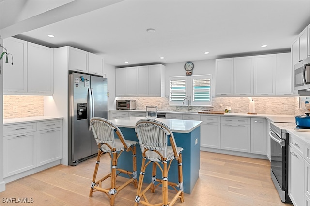 kitchen with a center island, stainless steel appliances, white cabinetry, and light hardwood / wood-style flooring