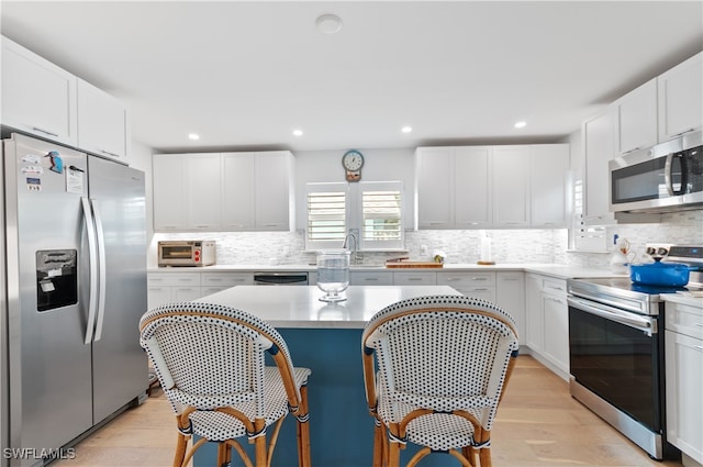 kitchen with a center island, white cabinets, decorative backsplash, light wood-type flooring, and appliances with stainless steel finishes