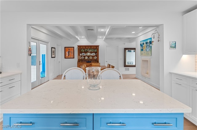 kitchen featuring beamed ceiling, a center island, light stone counters, and blue cabinets