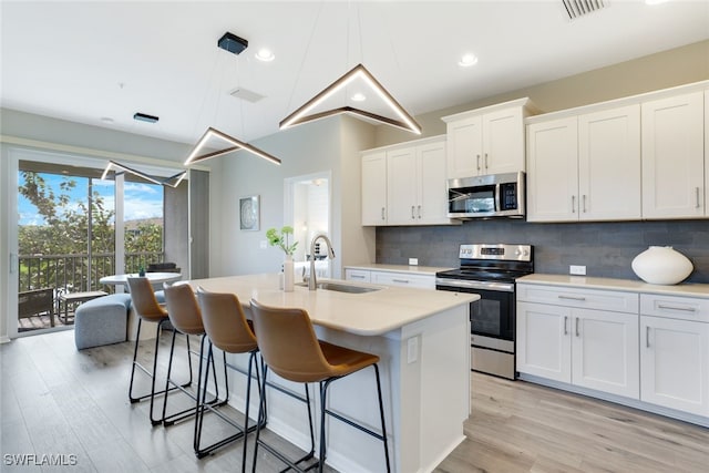 kitchen featuring an island with sink, sink, white cabinets, and stainless steel appliances