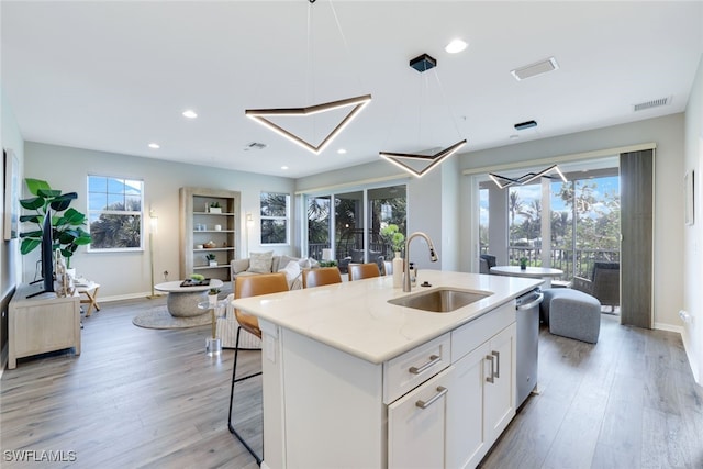 kitchen featuring white cabinetry, sink, hanging light fixtures, a center island with sink, and light wood-type flooring