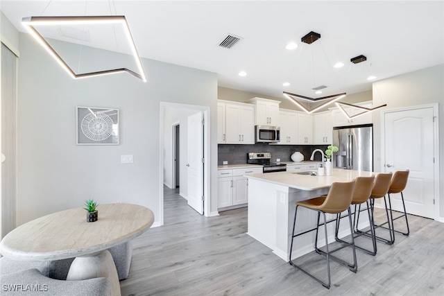 kitchen with backsplash, sink, light hardwood / wood-style flooring, appliances with stainless steel finishes, and white cabinetry