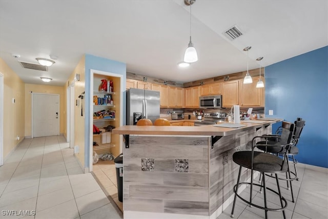 kitchen featuring light brown cabinets, hanging light fixtures, a breakfast bar area, kitchen peninsula, and stainless steel appliances