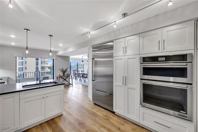 kitchen featuring white cabinetry, sink, decorative light fixtures, appliances with stainless steel finishes, and light wood-type flooring