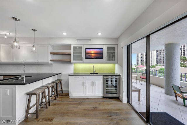 kitchen with pendant lighting, backsplash, wine cooler, light wood-type flooring, and white cabinetry