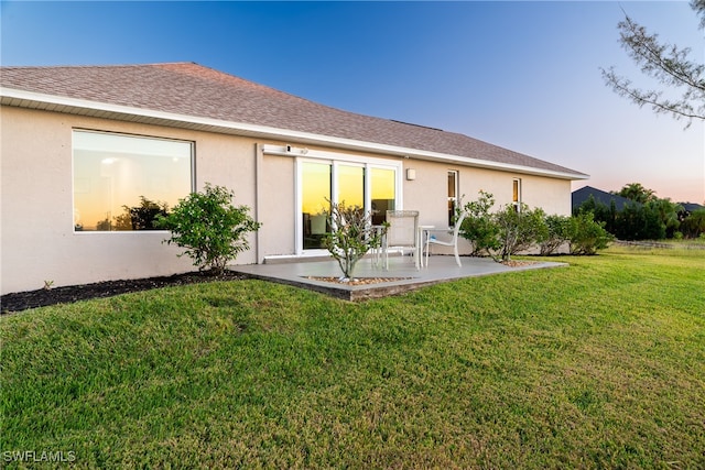 back house at dusk featuring a yard and a patio