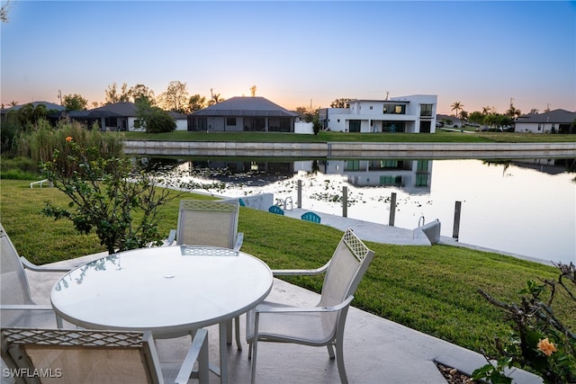 patio terrace at dusk featuring a yard and a water view