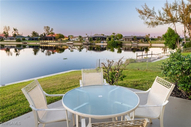 patio terrace at dusk featuring a water view and a yard