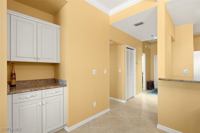 kitchen with crown molding, white cabinets, stone countertops, and light tile patterned floors