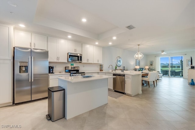 kitchen with pendant lighting, a center island, a tray ceiling, kitchen peninsula, and stainless steel appliances