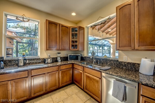 kitchen featuring plenty of natural light, sink, stainless steel appliances, and dark stone counters