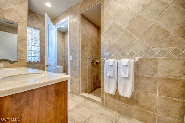 bathroom featuring a tile shower, vanity, and tile walls