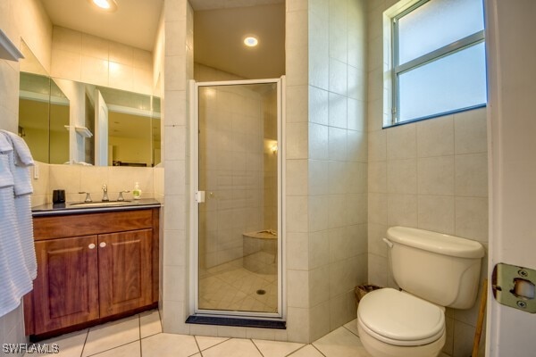 bathroom with tile patterned flooring, toilet, a shower with door, and tile walls