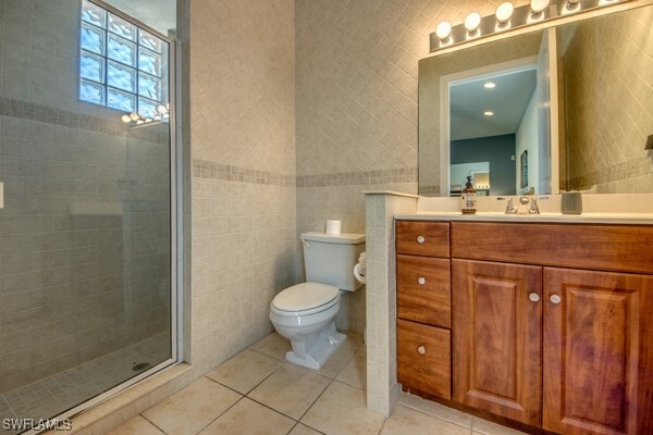 bathroom featuring tile patterned floors, vanity, a shower with shower door, and tile walls