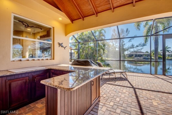 view of patio with a lanai, area for grilling, a water view, and a bar